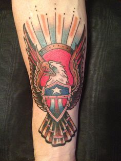 an eagle and shield tattoo on the left arm with sunbursts in the background