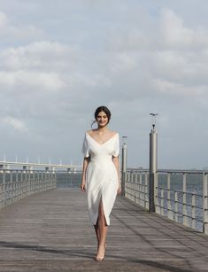 a woman in a white dress walking on a pier