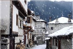 an alley way with snow falling on the ground and buildings in the background, surrounded by mountains