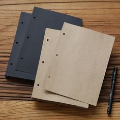 three pieces of brown paper sitting on top of a wooden table next to a pen