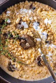 a close up of a bowl of soup with mushrooms and cheese on top, next to a spoon