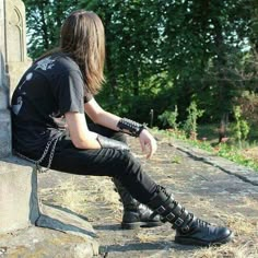 a man with long hair wearing black leather boots and chains sitting on a stone wall