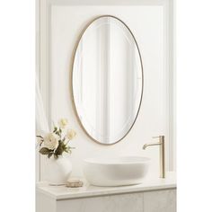 a white sink sitting under a mirror next to a vase with flowers in front of it