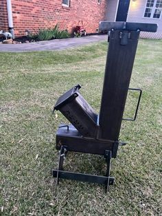 the back end of a black metal object sitting on top of green grass in front of a brick building