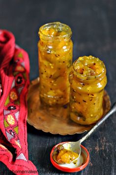 two jars filled with food sitting on top of a wooden tray next to a spoon