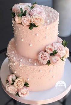 a three tiered pink wedding cake with flowers on the top and pearls on the bottom