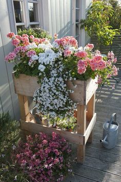 some pink and white flowers are in a wooden planter on a deck next to a watering can