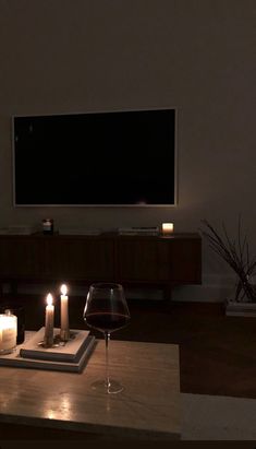 candles are lit in front of a flat screen tv and wine glass on a table