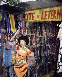 a woman standing in front of a store with lots of colorful items on display behind her