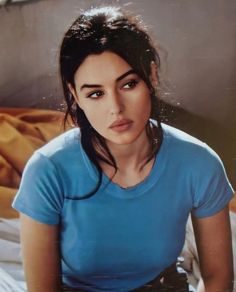 a woman sitting on top of a bed wearing a blue shirt