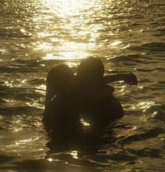 two people are in the water with their arms around each other as they swim towards the sun