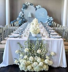 a table set up with white flowers and blue balloons