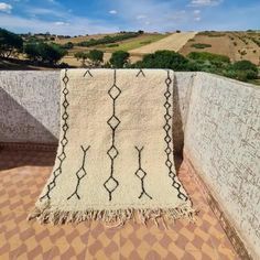 a blanket is hanging on the side of a wall in front of some hills and trees