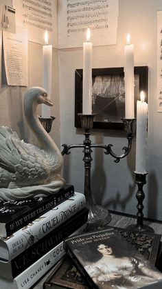 a swan statue sitting on top of a table next to some books and lit candles