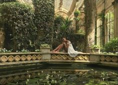 a bride and groom are sitting on the edge of a pond with lily pads in front of them