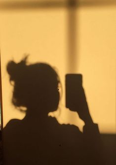 the shadow of a woman holding a cell phone in front of her face and looking at it