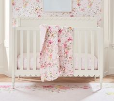 a white crib with pink flowers on the bedding and a mirror above it