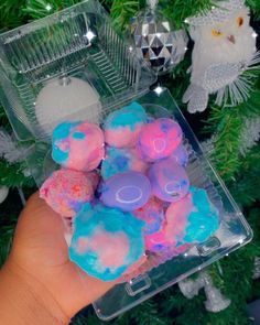 a hand is holding some soaps in front of a christmas tree with other ornaments