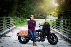 a man sitting on a motorcycle in the middle of a bridge with trees and grass behind him