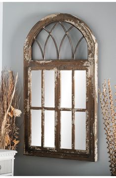 an old window frame mirror hanging on the wall next to a vase with dried flowers