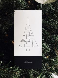 a christmas tree ornament hanging from the top of a fir tree with a black and white card that says happy holidays