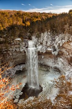 an aerial view of a waterfall with ice on the water and trees in the background