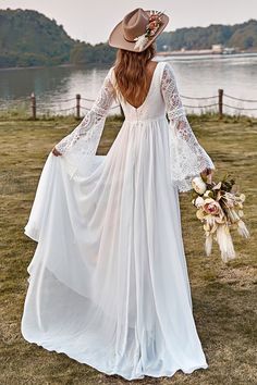 a woman in a long white dress and cowboy hat is standing on the grass with her back to the camera