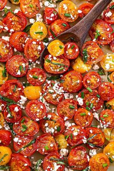 a pan filled with sliced tomatoes and topped with feta cheese, herbs and a wooden spoon