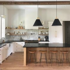 a large kitchen with white cabinets and black counter tops, two pendant lights hanging over the island