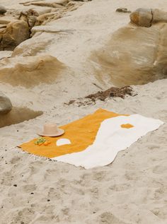 an orange and white blanket on the beach with a hat sitting on top of it