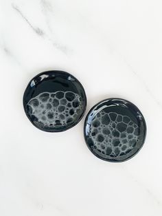 two black plates sitting on top of a white counter next to each other with bubbles in them