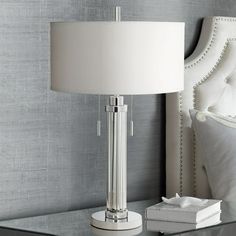 a white lamp sitting on top of a glass table next to a night stand with a book