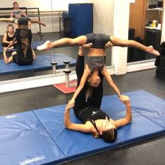 two people doing acrobatic exercises on blue mats in a gym with other people