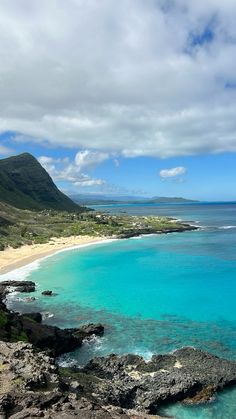 the ocean is clear and blue as it sits next to some rocky shore with mountains in the background