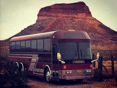 a red bus parked in front of a large rock formation on the side of a road