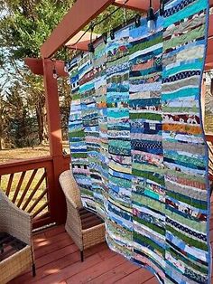 a quilt hanging from a wooden deck in front of some wicker chairs and a table