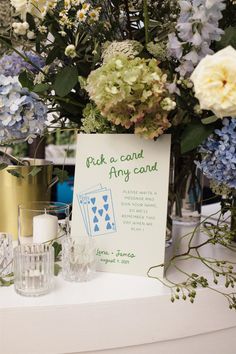 a table topped with flowers and cards on top of a white table cloth next to candles