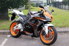 an orange and black motorcycle is parked on the side of the road in front of a chain link fence