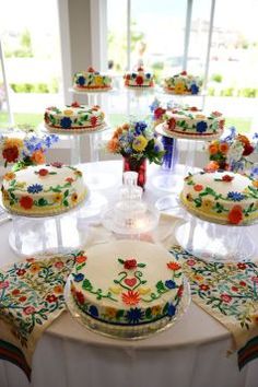 a table topped with lots of cakes covered in frosted icing and colorful flowers