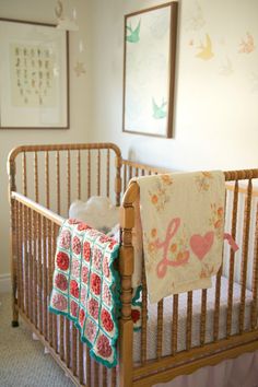 a baby crib with a blanket hanging from it's side and two pictures on the wall