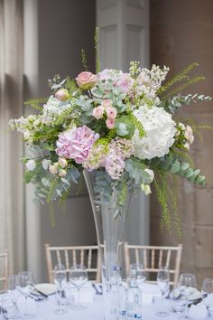 a tall vase filled with lots of flowers on top of a white table covered in blue linens