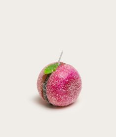 a pink apple with a green leaf on it's side and a white stick sticking out of the top