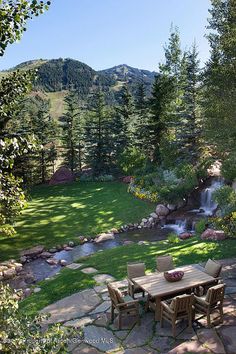 a table and chairs in the middle of a yard with a stream running through it