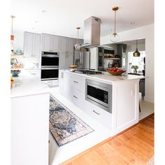 a kitchen with white cabinets and stainless steel appliances, wood flooring and an area rug