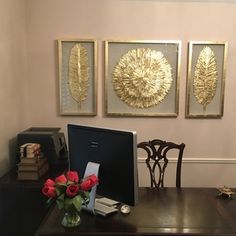 a desk with a laptop and flowers on it in front of three framed art pieces