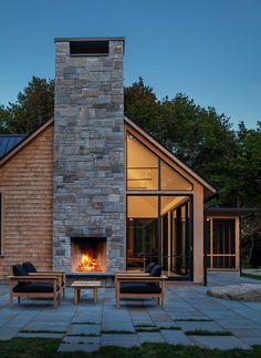 an outdoor fireplace in the middle of a patio with two chairs and tables next to it