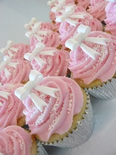 cupcakes with pink frosting and white bows on them are arranged in rows