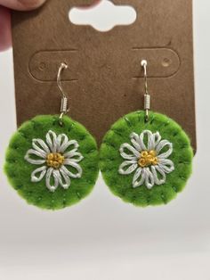 a pair of green and white earrings with flowers on the front, sitting next to a card