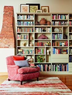 a living room filled with lots of books on top of a book shelf next to a red chair