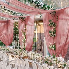 a long table with white chairs and pink drapes draped over it for a wedding reception